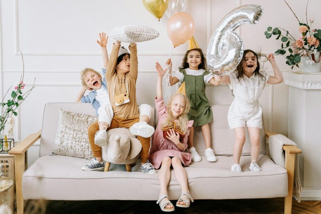 Happy kids celebrating a birthday with balloons and excitement on a living room sofa.